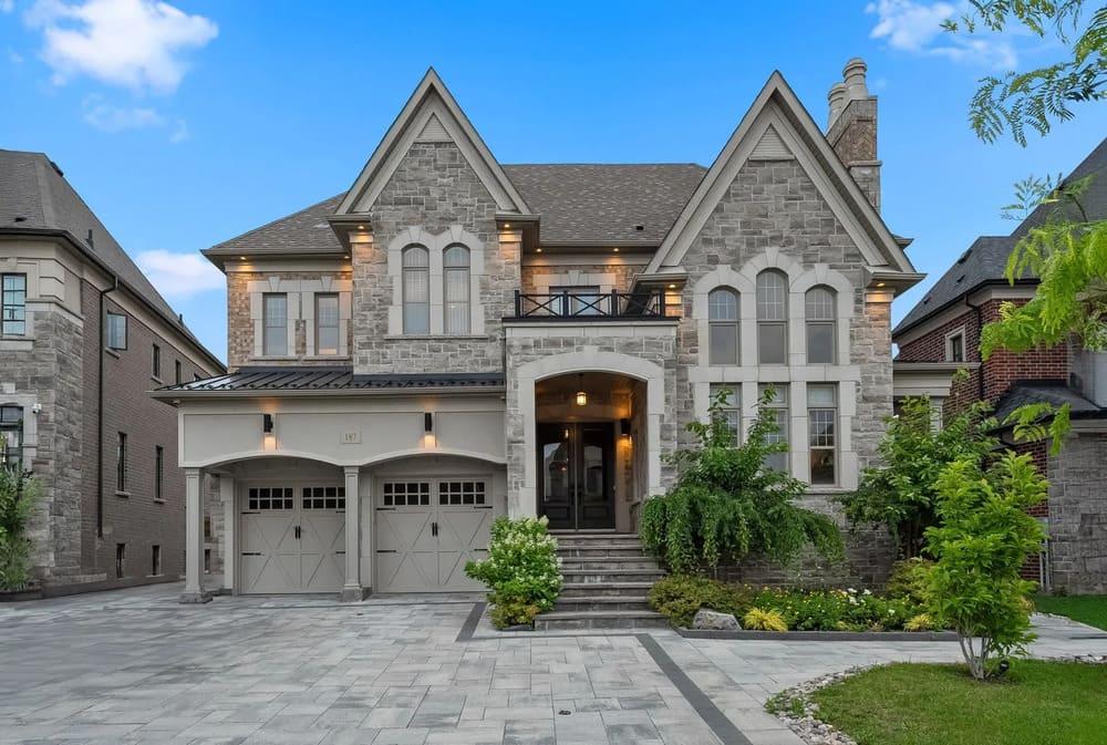 Two-story stone house with arched windows, double garage, front steps, and landscaped yard under a clear blue sky.