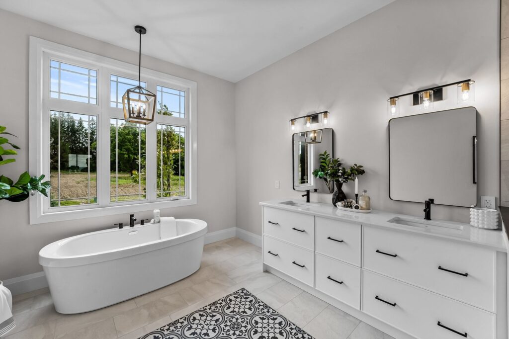 Modern bathroom with a freestanding bathtub, double vanity sinks with black fixtures, large mirrors, patterned floor tiles, and a large window overlooking greenery.