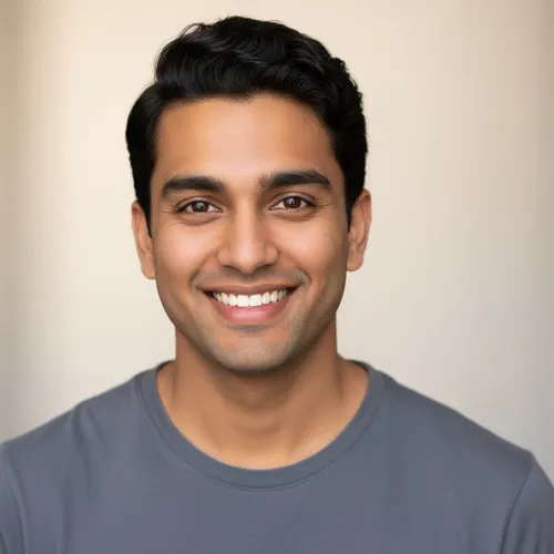 A man with short dark hair wearing a gray t-shirt smiles at the camera against a neutral background.