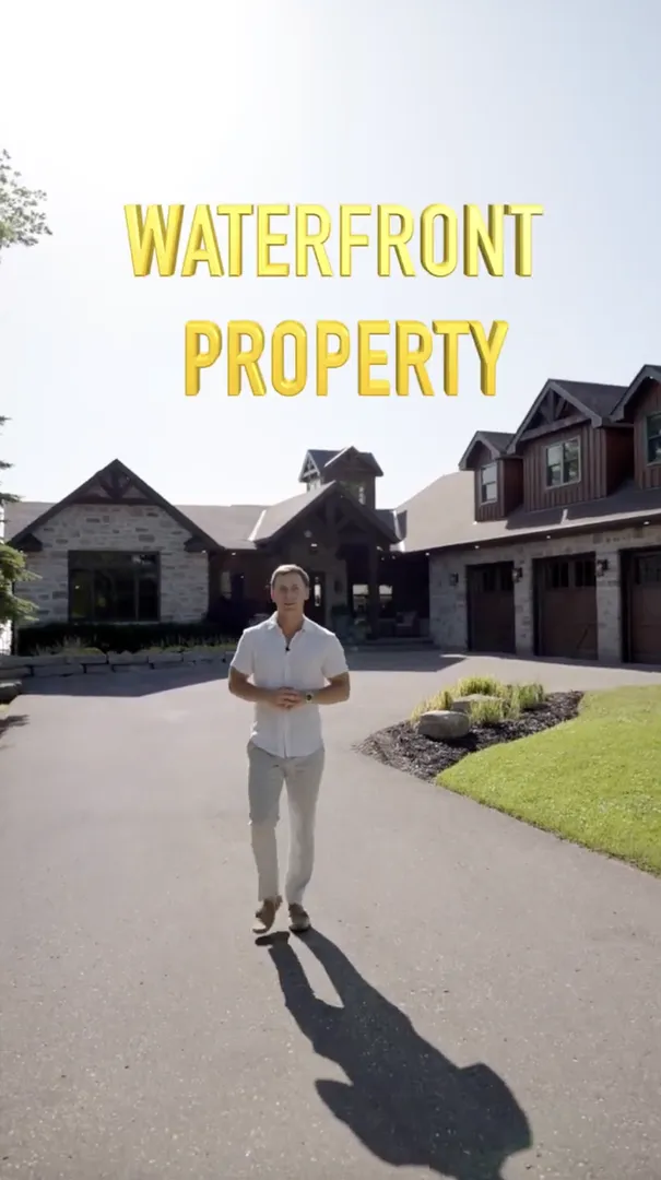 A man stands in front of a large stone and wood house with the text "Waterfront Property" above him.